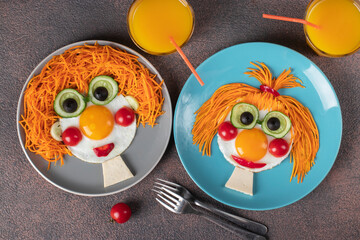 Fun Food for kids - smiling faces boy and girl made from fried eggs, carrot, cucumbers, crerry tomato, black olives on plates. Creative healthy breakfast for children, Top view