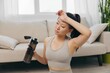 © SHOTPRIME STUDIO - Asian woman at home doing stretching and yoga online and drinking water while resting, wiping sweat from her forehead