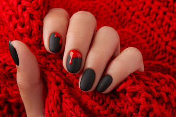 Close up womans hand with halloween manicure on red background holding fabric. Manicure, pedicure beauty salon concept