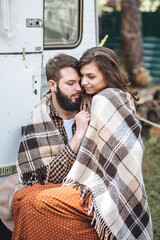 Wall Mural - Young beautiful loving couple travelling across country in the van. Millennial man and woman in a travel camper. Cozy atmosphere, vacations vibe. Drinking tea, playing guitar