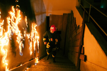 Brave Fireman Descends Stairs of a Burning Building and Holds Saved Girl in His Arms. Open fire and one Firefighter in the Background.