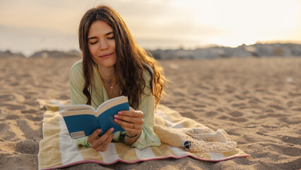 Canvas Print - Pretty young attractive woman reading book on the blur background. European brunette lying at beach in morning. Leisure of life concept