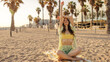 © Look! - Cheerful dark-haired woman smiling with close eyes relaxing and sitting on towel at sand. Wearing green linen costume, yellow swimwear. Rest time concept