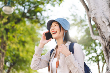 Wall Mural - Young adult asian woman traveller wear blue hat and backpack using mobile phone internet for calling on travel.