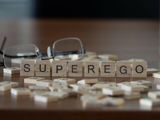 Sticker - superego word or concept represented by wooden letter tiles on a wooden table with glasses and a book