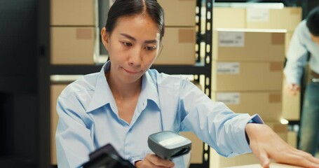 Wall Mural - Happy Asian girl and man partner wear formal shirt sit front desk computer use barcode machine scan record customer online data in cardboard box delivery at warehouse. Startup small business concept.