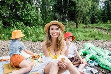 Smiling Woman Holding Ice Cream Sitting With Sons On Picnic