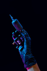 Wall Mural - Closeup of tattooer master's hand in black glove holding machine for making tattoo art on body isolated on dark background in neon light.