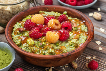 Wall Mural - Healthy breakfast. Oatmeal matcha porridge with fresh raspberries, caramel sauce and pistachios in a bowl