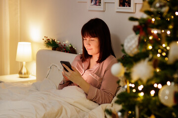 Wall Mural - young woman using smartphone in decorated bedroom with christmas tree