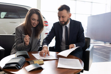 Wall Mural - young woman buys a new car in a car dealership and signs documents, car insurance concept