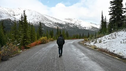 Wall Mural - Man traveler walking in snowing on the road with canadian rockies at national park