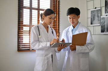 Two expert young Asian female and male doctors in a white gown are talking in the office.