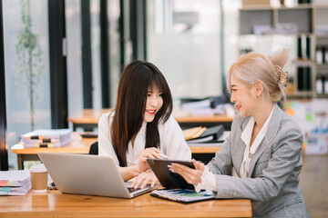 Two Asian businesswoman discuss investment project working and planning strategy with tablet laptop computer in modern office..