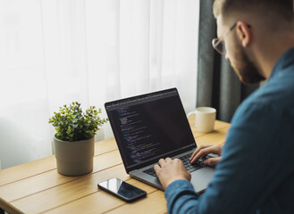 Man coding on laptop on a desk, remote working from home