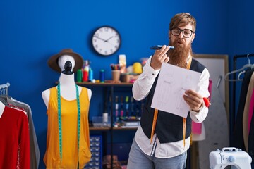 Poster - Young redhead man tailor talking on smartphone reading document at clothing factory