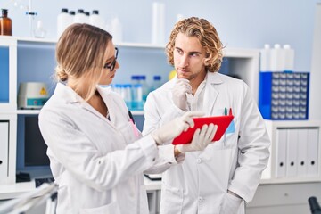 Wall Mural - Man and woman wearing scientist uniform using touchpad at laboratory