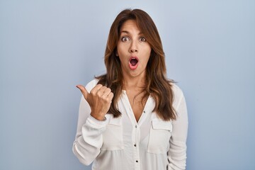 Poster - Hispanic woman standing over isolated background surprised pointing with hand finger to the side, open mouth amazed expression.