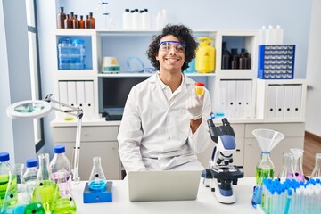 Poster - Young hispanic man wearing scientist uniform using laptop analysing urine test tube at laboratory