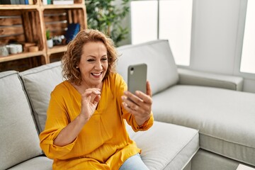 Canvas Print - Middle age caucasian woman having video call using smartphone sitting on the sofa at home.