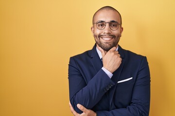 Poster - Hispanic man with beard wearing suit and tie looking confident at the camera with smile with crossed arms and hand raised on chin. thinking positive.