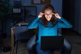 Fototapeta Tulipany - Brunette woman working at the office at night covering ears with fingers with annoyed expression for the noise of loud music. deaf concept.