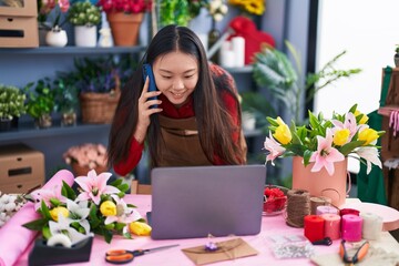 Sticker - Young chinese woman florist talking on smartphone using laptop at flower shop