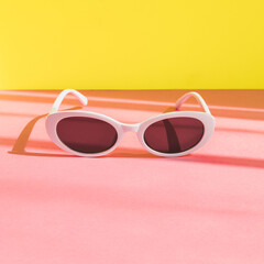 Wall Mural - women's sunglasses in a white frame on a yellow and pink background. minimalism and pop art style.