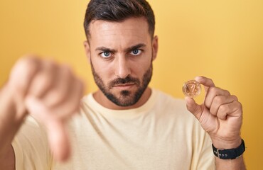 Wall Mural - Handsome hispanic man holding tron cryptocurrency coin with angry face, negative sign showing dislike with thumbs down, rejection concept