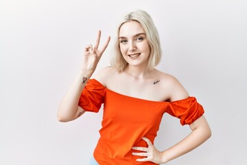 Sticker - Young caucasian woman standing over isolated background smiling looking to the camera showing fingers doing victory sign. number two.