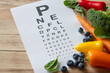 Food for eyes health, colorful vegetables and fruits, rich in lutein and eye test chart on wooden background, concept