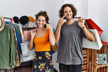 Wall Mural - Young hispanic couple holding shopping bags at retail shop pointing with hand finger to face and nose, smiling cheerful. beauty concept