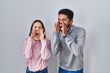 Wall Mural - Young hispanic couple standing together shouting angry out loud with hands over mouth