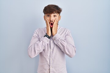 Sticker - Arab man with beard standing over blue background afraid and shocked, surprise and amazed expression with hands on face