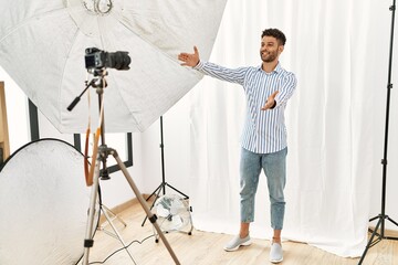 Wall Mural - Arab young man posing as model at photography studio looking at the camera smiling with open arms for hug. cheerful expression embracing happiness.