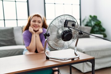 Wall Mural - Young redhead woman smiling confident using electric ventilator at home