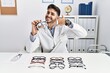 Young optician man holding optometry glasses smiling doing phone gesture with hand and fingers like talking on the telephone. communicating concepts.