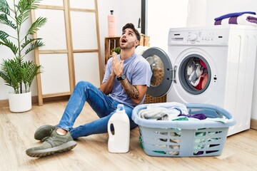 Sticker - Young hispanic man putting dirty laundry into washing machine begging and praying with hands together with hope expression on face very emotional and worried. begging.