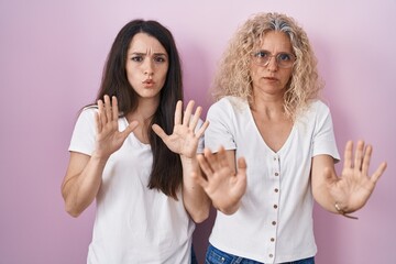 Poster - Mother and daughter standing together over pink background moving away hands palms showing refusal and denial with afraid and disgusting expression. stop and forbidden.