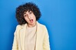 © Krakenimages.com - Young brunette woman with curly hair standing over blue background in shock face, looking skeptical and sarcastic, surprised with open mouth