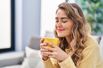 Poster - Young woman drinking coffee sitting on sofa at home