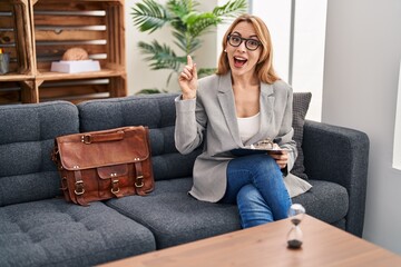 Canvas Print - Hispanic woman working at consultation office pointing finger up with successful idea. exited and happy. number one.