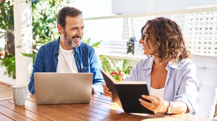 Wall Mural - Middle age hispanic couple reading book and using laptop at terrace