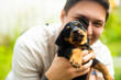 a young guy is playing with a black brown puppy hunting terrier dog