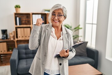 Poster - Middle age woman with grey hair at consultation office very happy and excited doing winner gesture with arms raised, smiling and screaming for success. celebration concept.