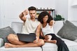 © Krakenimages.com - Young interracial couple using laptop at home sitting on the sofa looking unhappy and angry showing rejection and negative with thumbs down gesture. bad expression.