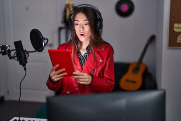 Wall Mural - Young brunette woman singing song using microphone scared and amazed with open mouth for surprise, disbelief face