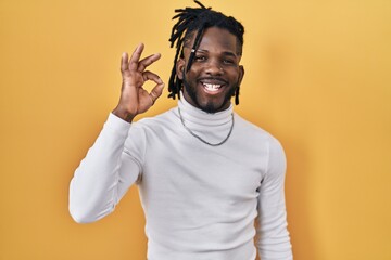 Sticker - African man with dreadlocks wearing turtleneck sweater over yellow background smiling positive doing ok sign with hand and fingers. successful expression.