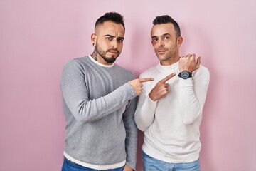 Canvas Print - Homosexual couple standing over pink background in hurry pointing to watch time, impatience, looking at the camera with relaxed expression