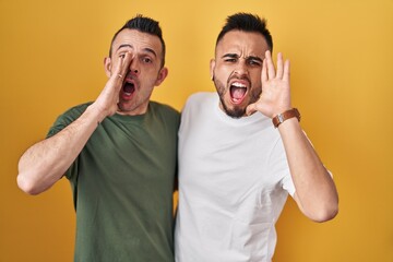 Sticker - Homosexual couple standing over yellow background shouting and screaming loud to side with hand on mouth. communication concept.